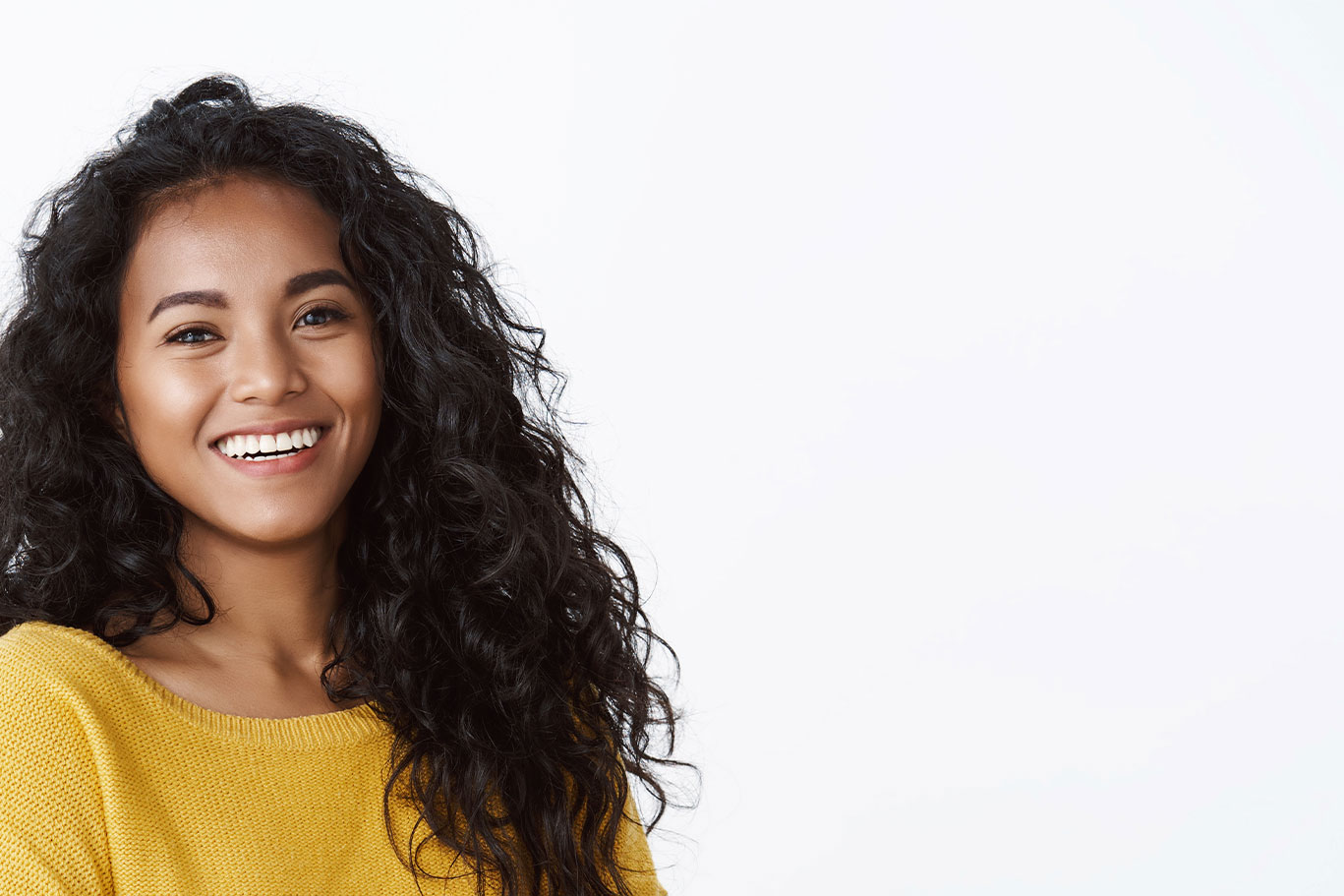 A smiling woman with long hair, wearing a yellow top, against a white background.