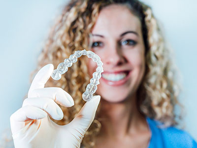 A woman holding a transparent dental retainer with a smile.