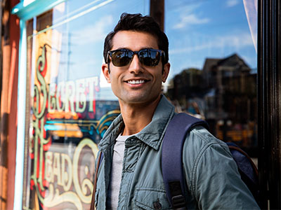A man with sunglasses and a backpack, standing outdoors in front of a store window.