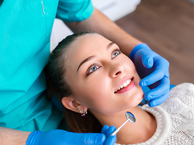 A dental hygienist is performing a teeth cleaning procedure on a woman who is smiling and looking at the camera, with a focus on oral health care.