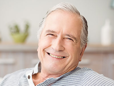 A smiling older man with white hair, wearing glasses, seated comfortably with his hands resting on his chest.